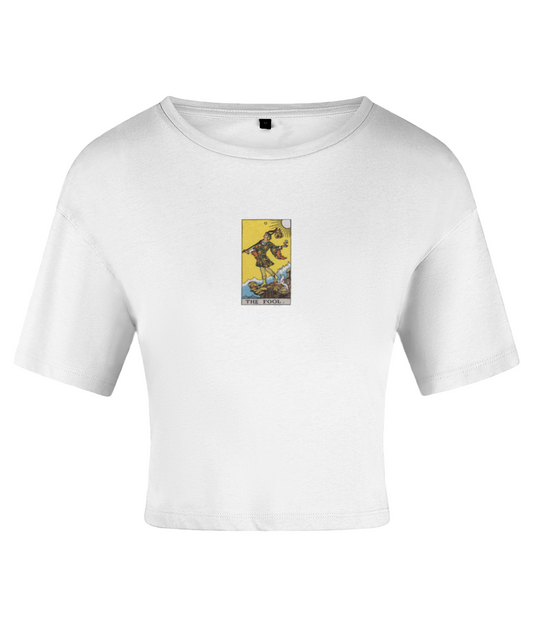 A white crop top with a tarot card graphic featuring the 'Fool' card in yellow and brown tones. On a white backdrop.